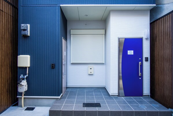 Ingresso di un edificio con una porta blu, un basculante bianco e un contatore dell'utenza sulla parete.