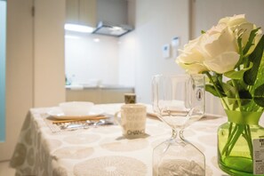 Un tavolo da pranzo con una tovaglia bianca, un vaso verde con fiori bianchi e un bicchiere di vetro trasparente.