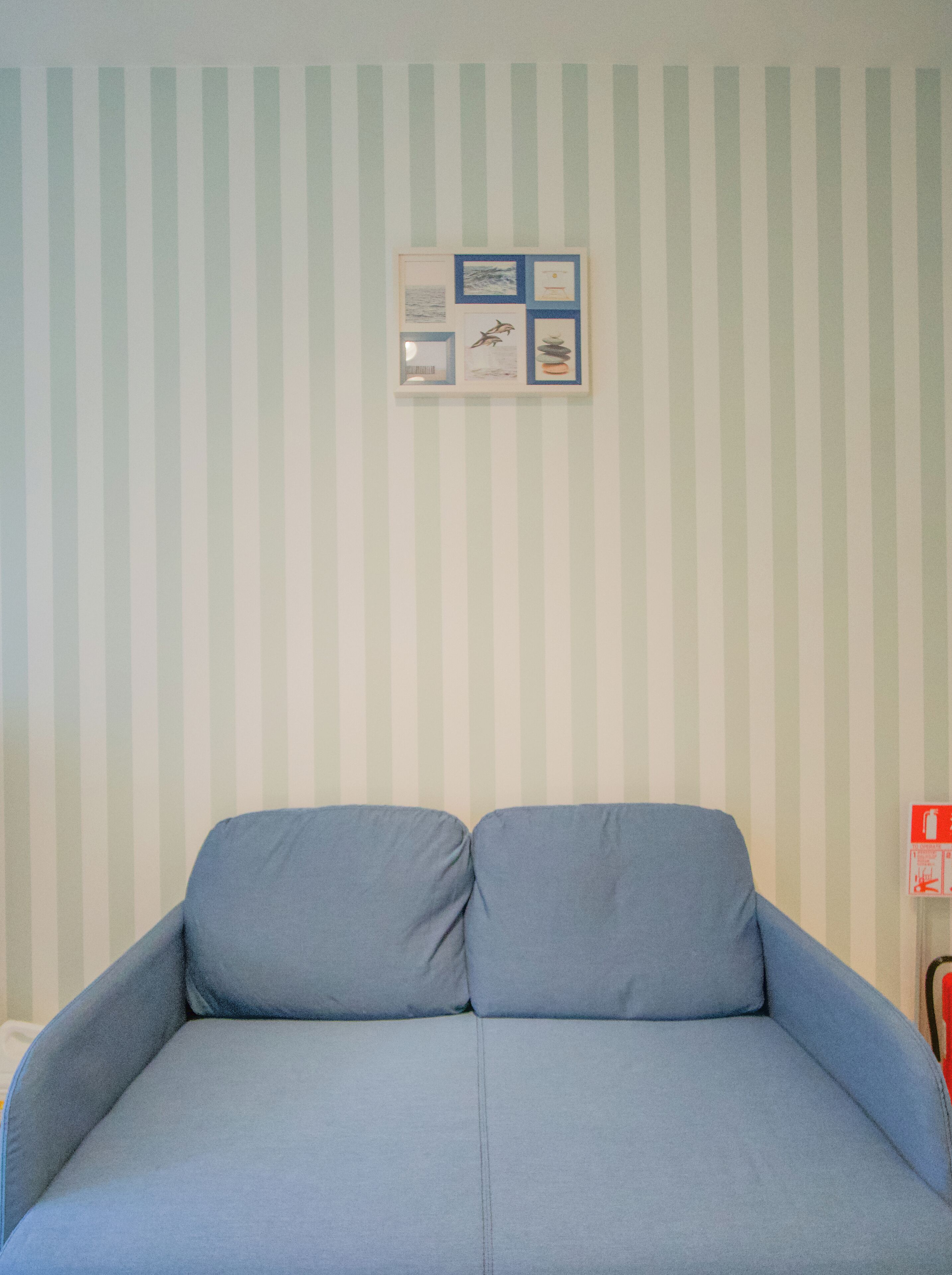 A room with a striped wall, a framed picture, and a blue sofa.
