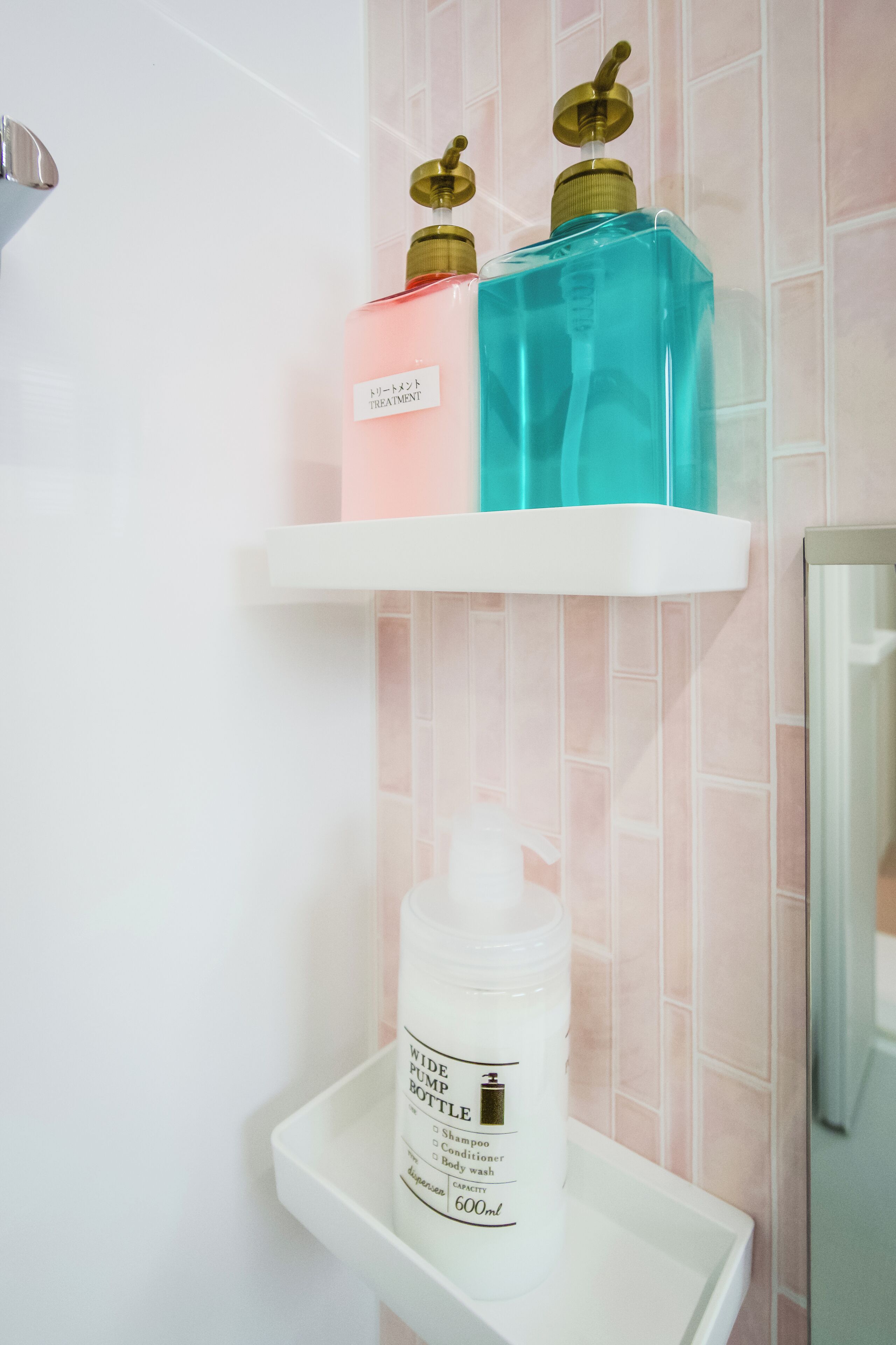 Une salle de bain avec un lavabo blanc, un miroir et deux étagères où sont rangées des bouteilles de shampoing et d’après-shampoing.