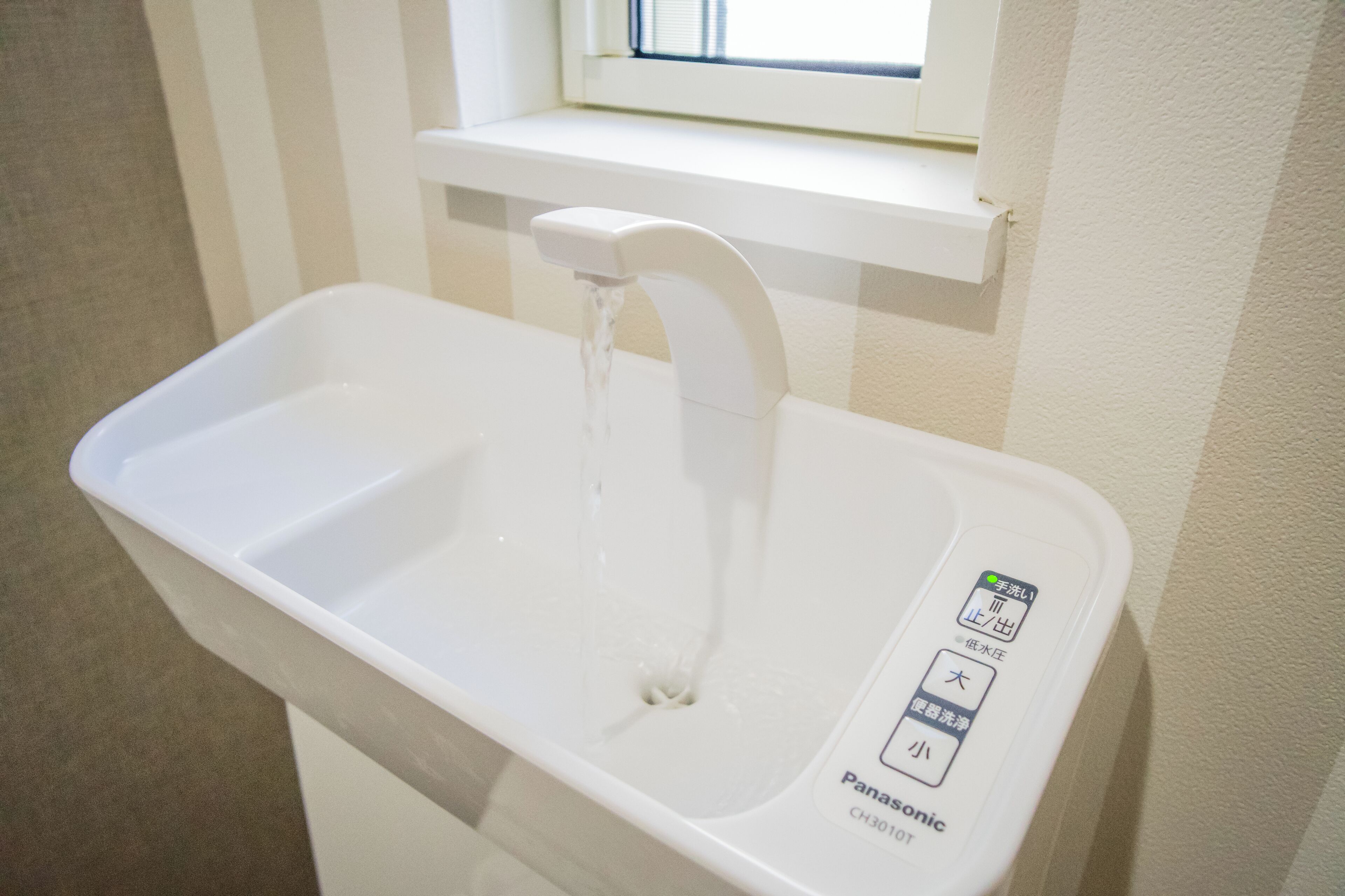 A white Panasonic sink with a faucet, a control panel with Japanese characters, and a window above the sink.