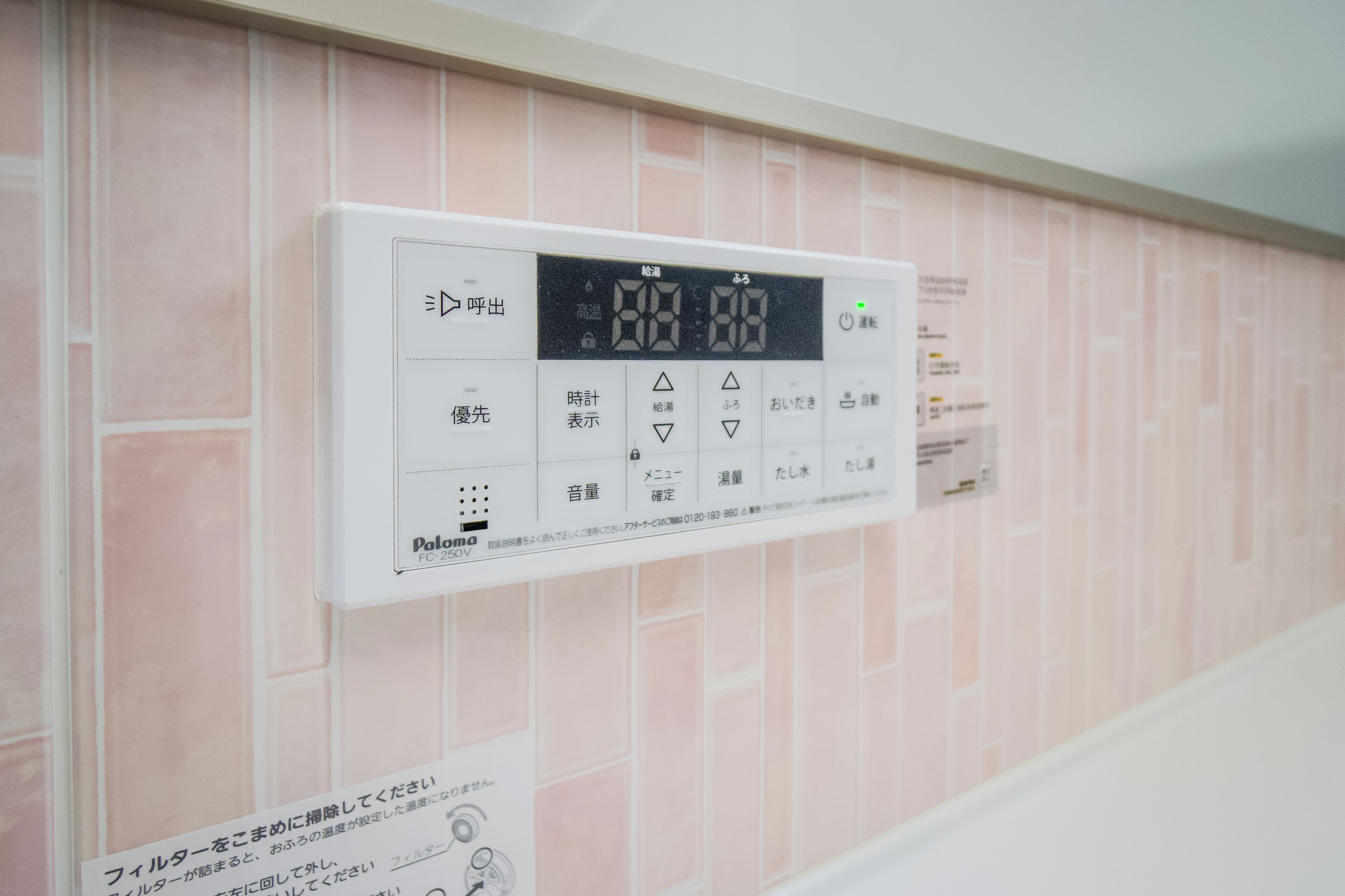 Un thermostat numérique fixé au mur, sur lequel on peut voir un motif de carreaux roses.