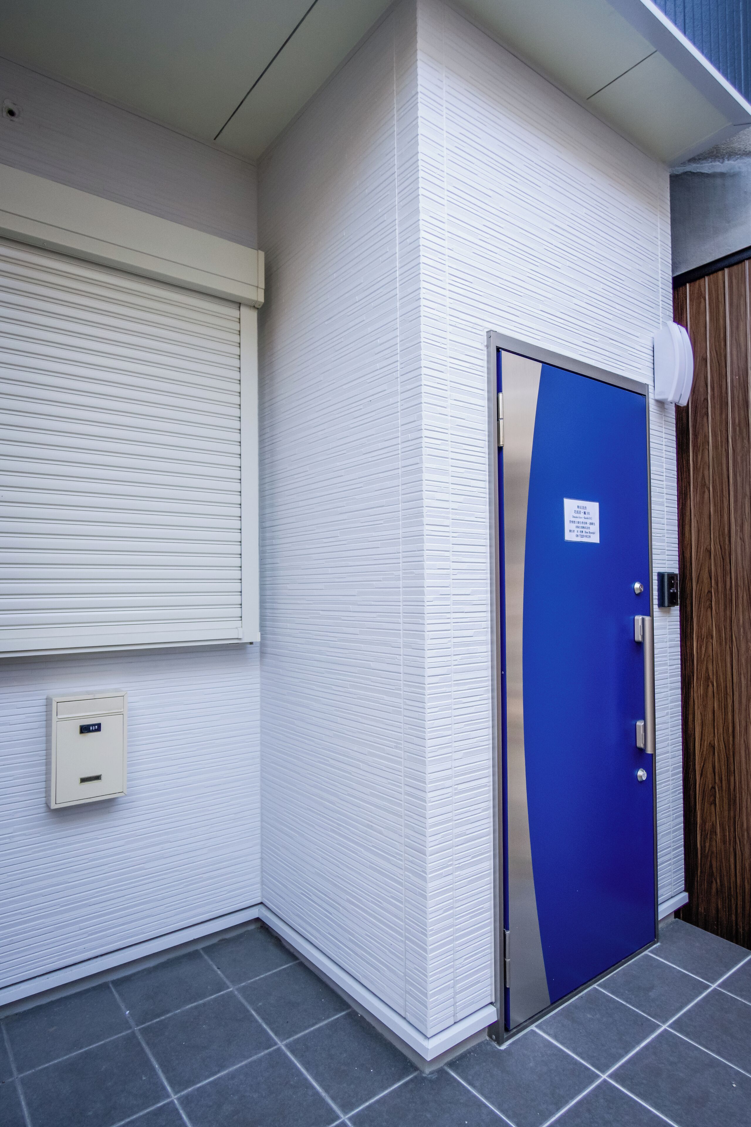 A blue door with a sign, a white textured wall, and a window with blinds.