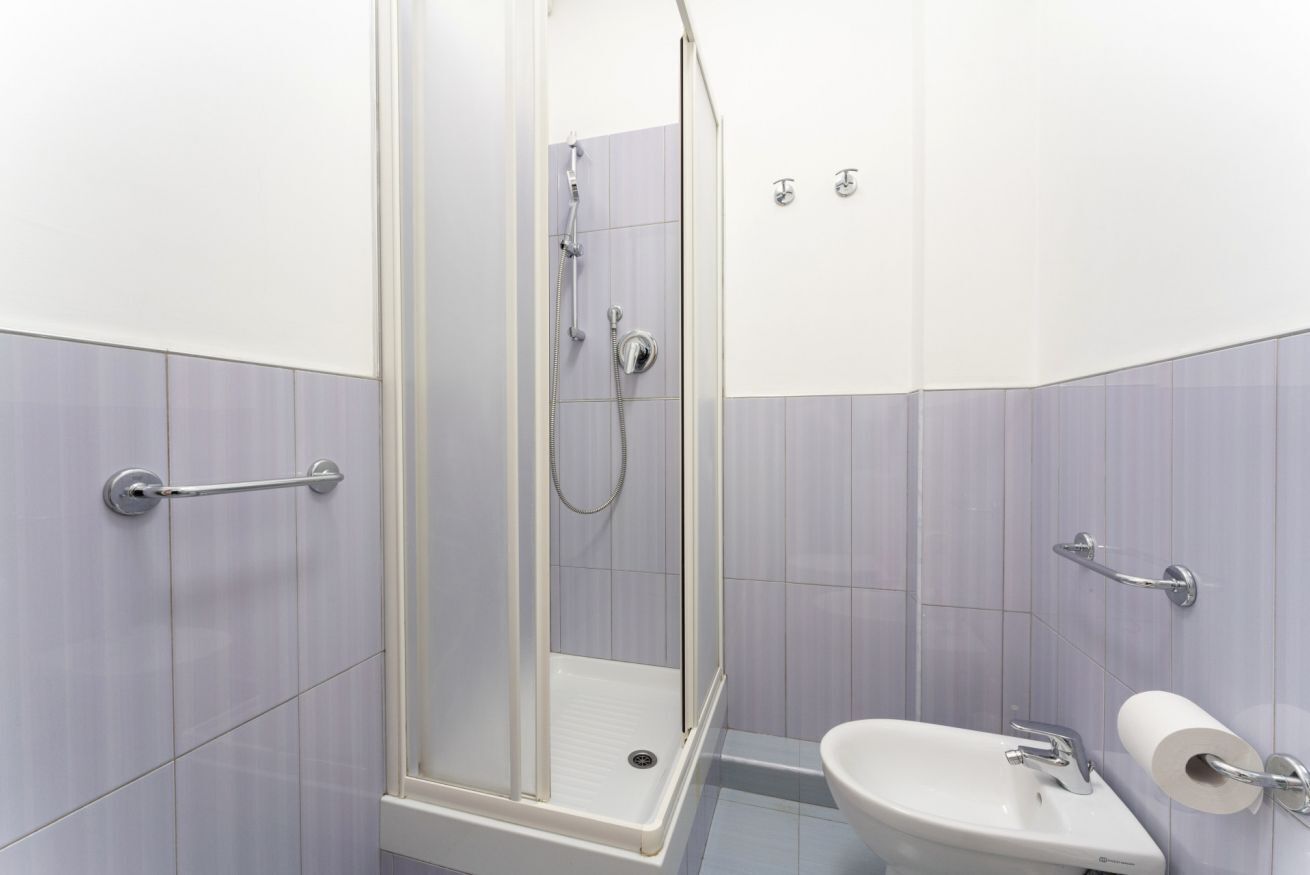 A bathroom with a shower, toilet, and sink, featuring a tiled wall and a handrail.