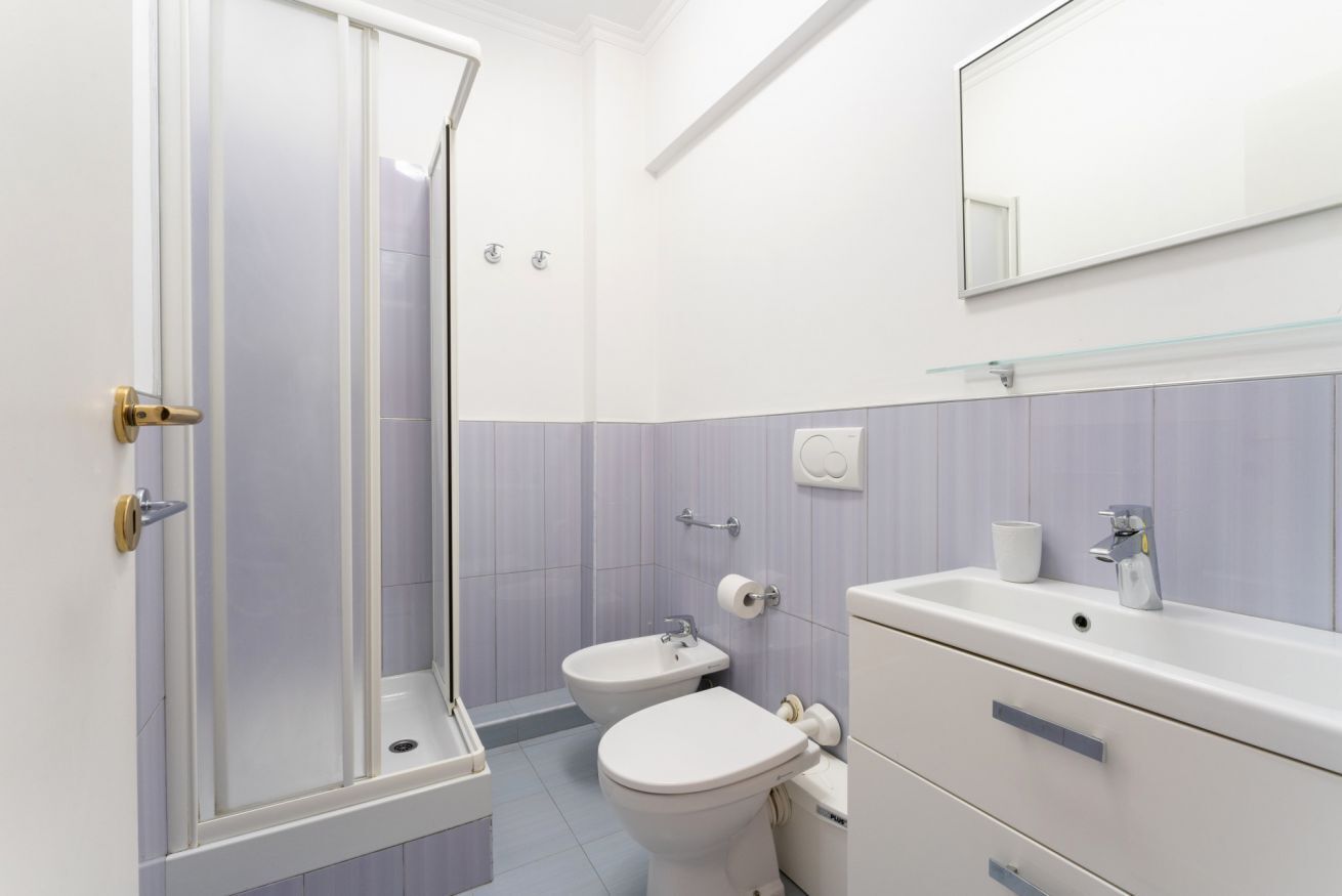 A bathroom with a shower, bidet, toilet, sink, and mirror.