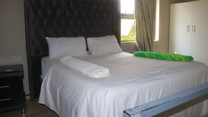 Un lit bien fait, avec du linge de lit blanc, une tête de lit sombre et un coussin vert.