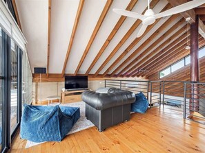 A spacious loft bedroom with a wooden ceiling, a large window, a bed, and a TV.
