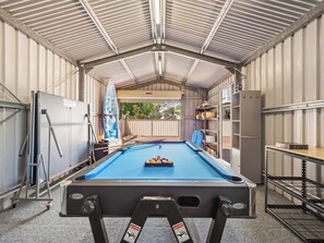 An indoor pool table with a blue felt surface, surrounded by metal shelving and a white door.