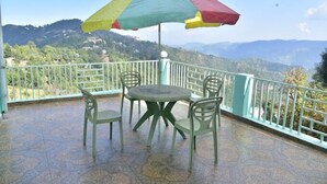A balcony with a table and chairs, an umbrella, and a scenic mountain view. - The Wild Cliff (Dhari)