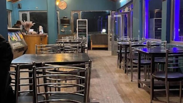A restaurant with wooden ceiling beams, blue walls, and tables with chairs. - The Wild Cliff (Dhari)