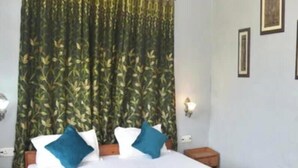 A bedroom with a large bed, a wooden headboard, a blue bedspread, and a green leafy curtain. - The Wild Cliff (Dhari)
