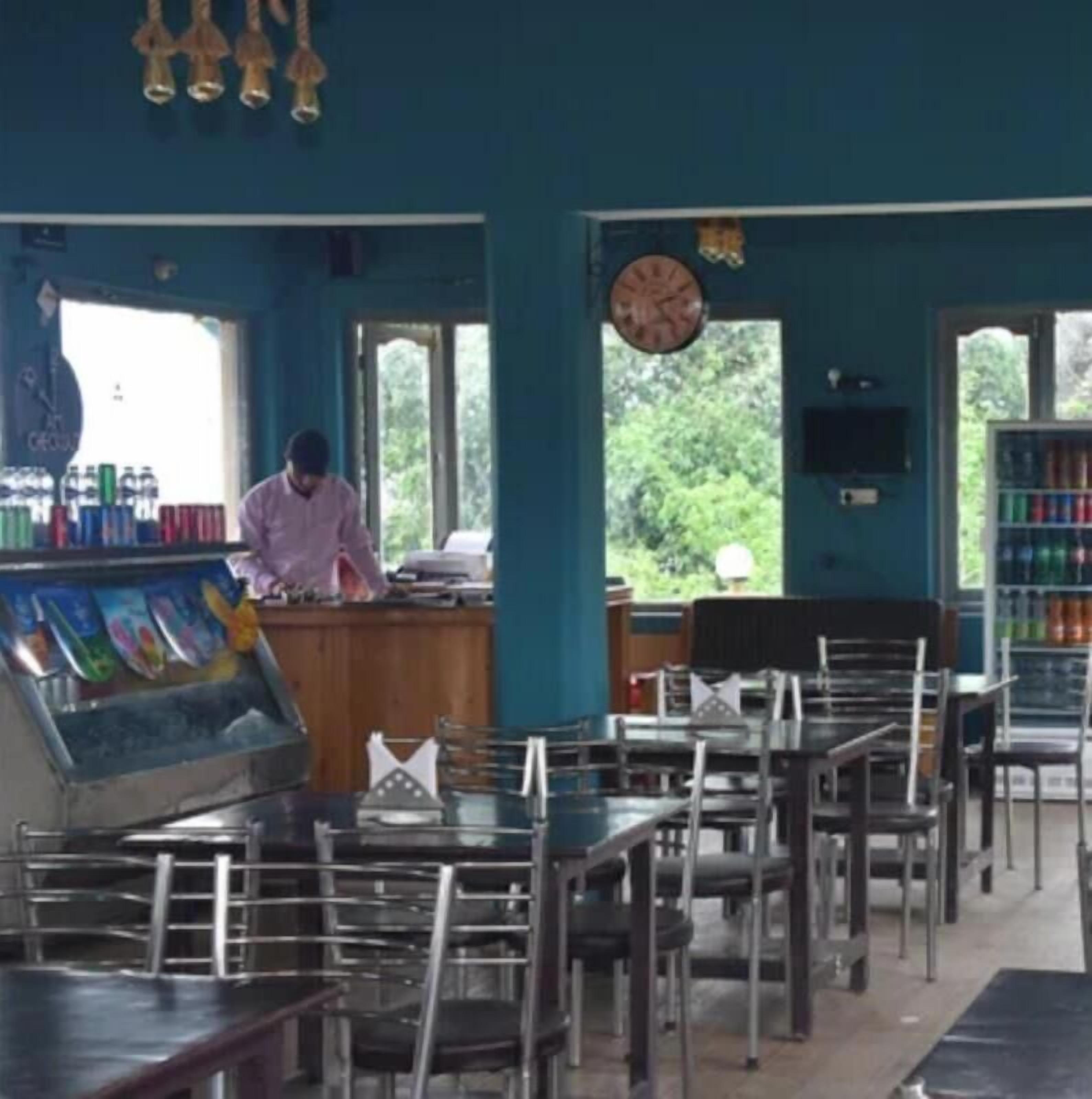 A restaurant with a counter, tables, chairs, and a clock on the wall.