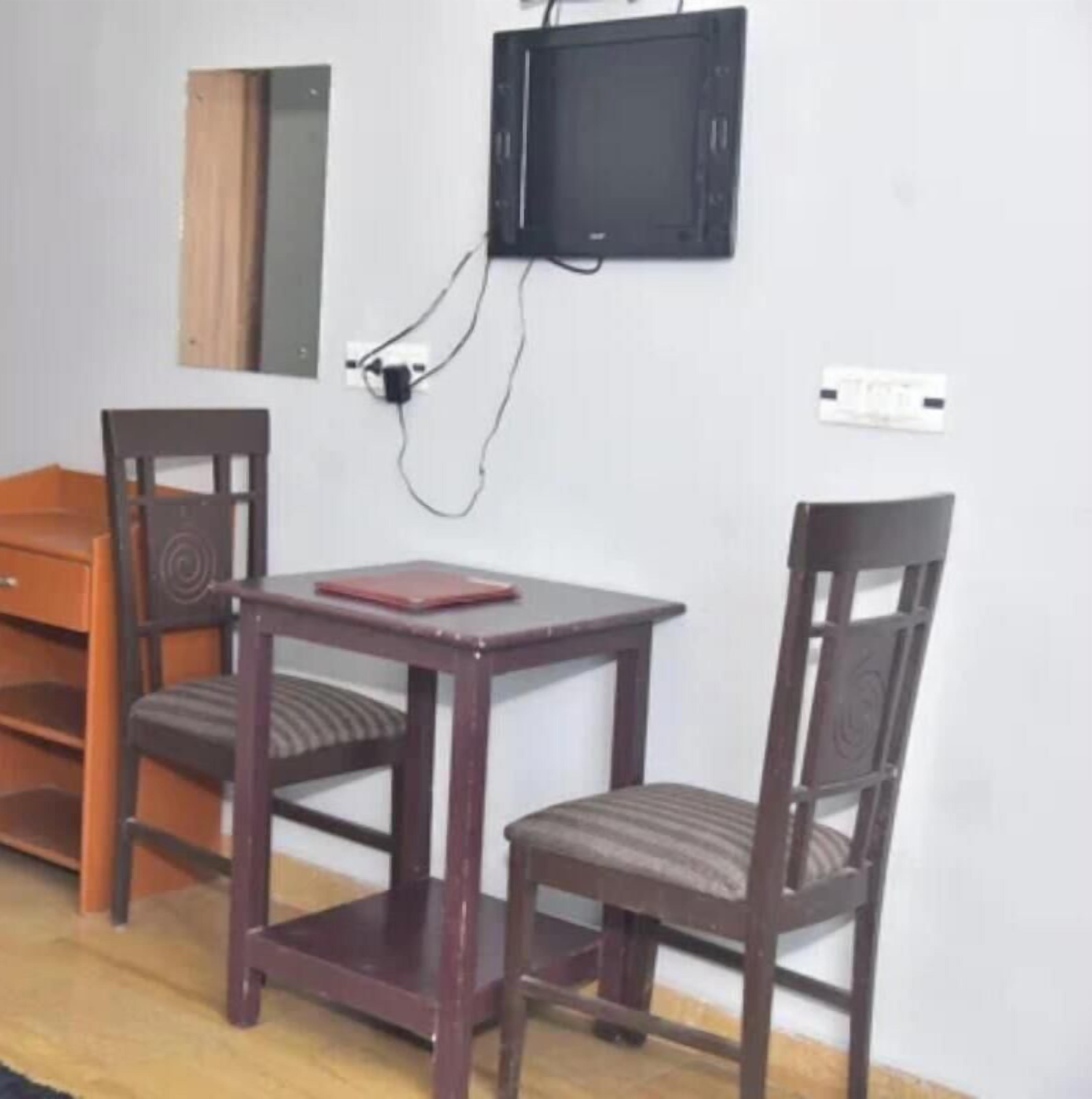 A small room with a wooden table and two chairs, a television mounted on the wall, and a power outlet.