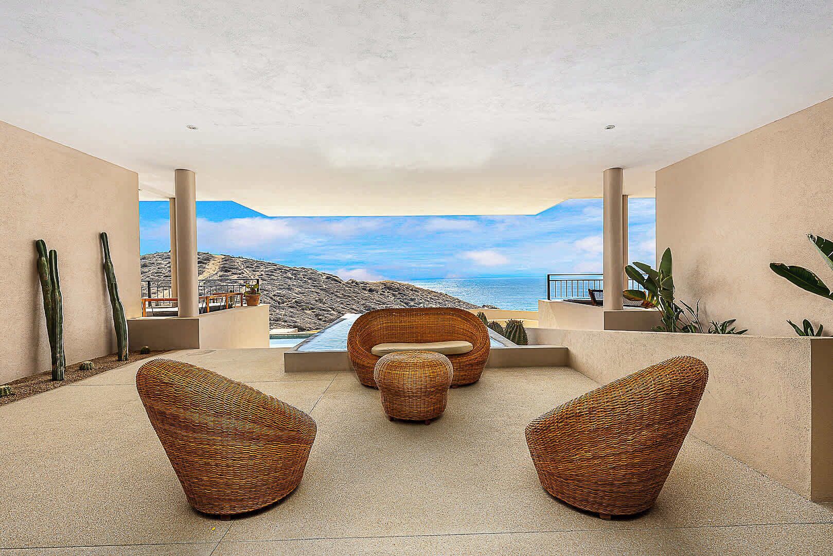 A modern outdoor seating area with wicker furniture, a pool, and a view of the ocean.