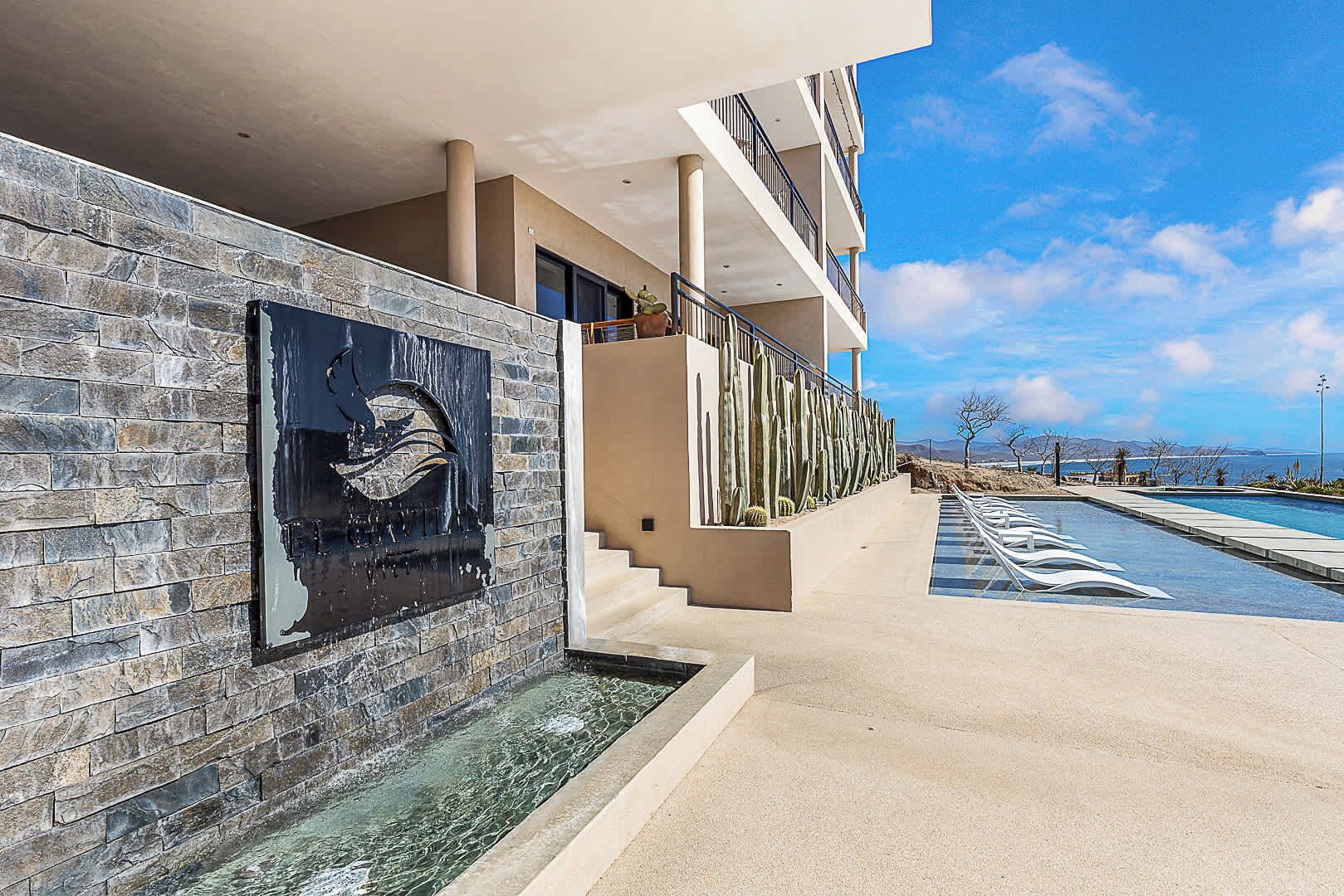 A modern hotel with a stone facade, a pool, and a view of the ocean.