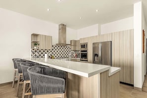 A modern kitchen with a central island, bar stools, built-in appliances, and a patterned backsplash.