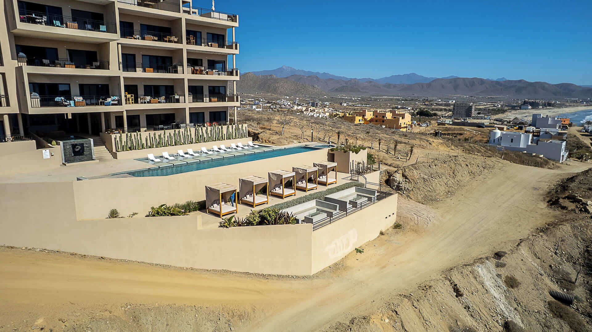 A hotel with a pool area, multiple balconies, and a view of the surrounding landscape.