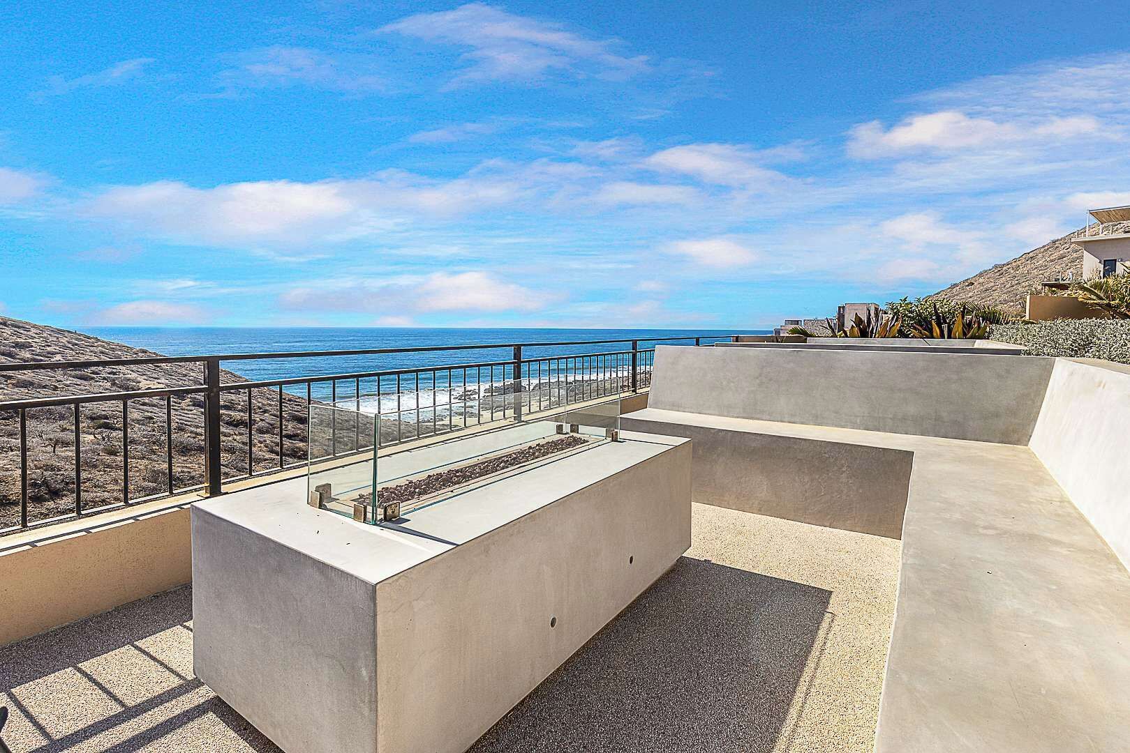 Une terrasse sur le toit, dotée d’un sol en béton, d’une rambarde en métal et offrant une vue sur la plage et l’océan.