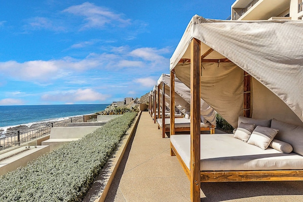 A seaside hotel with outdoor seating areas, a concrete pathway, and a view of the ocean.