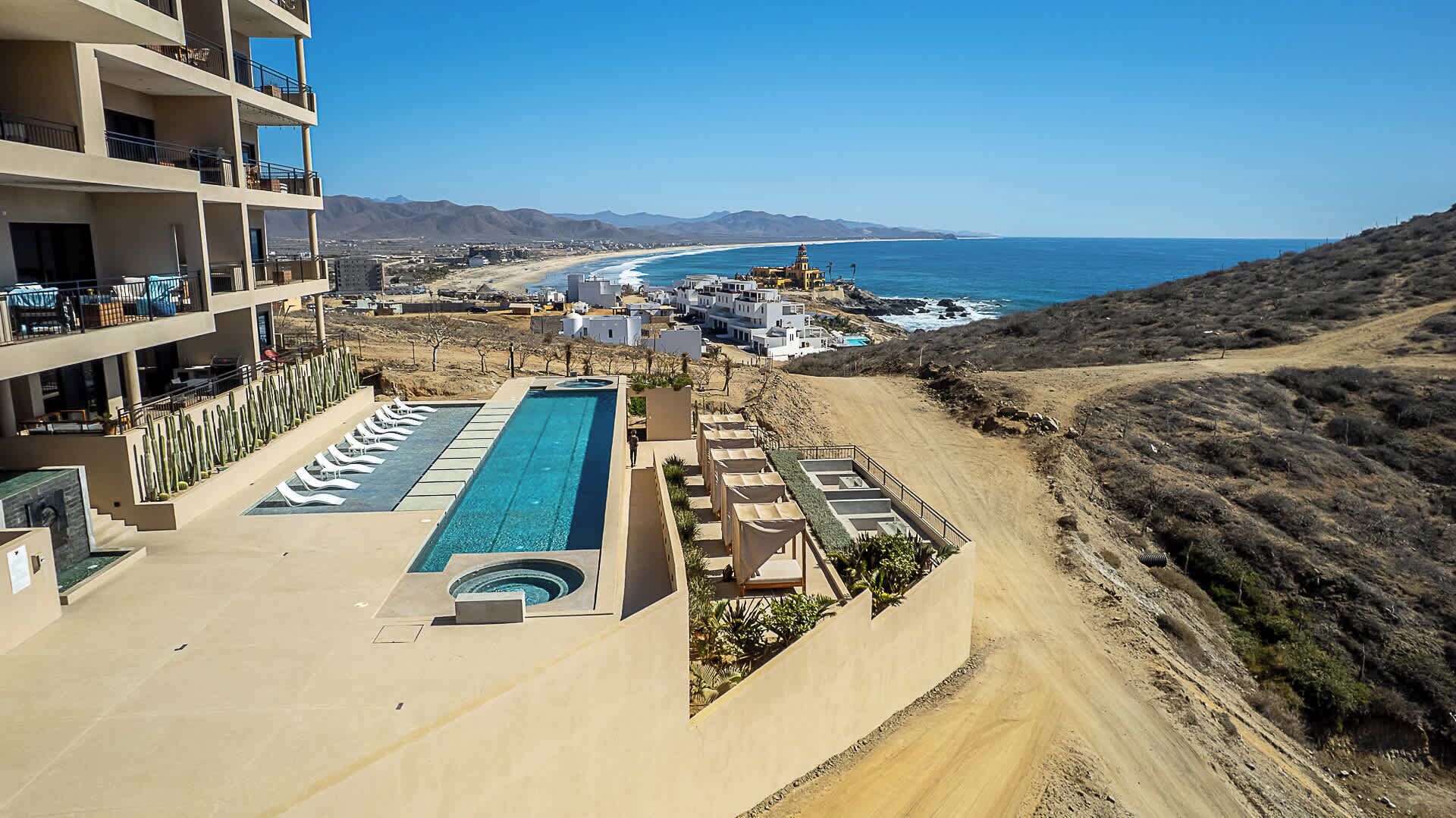 Een resort met een zwembad, meerdere balkons en uitzicht op strand en zee.