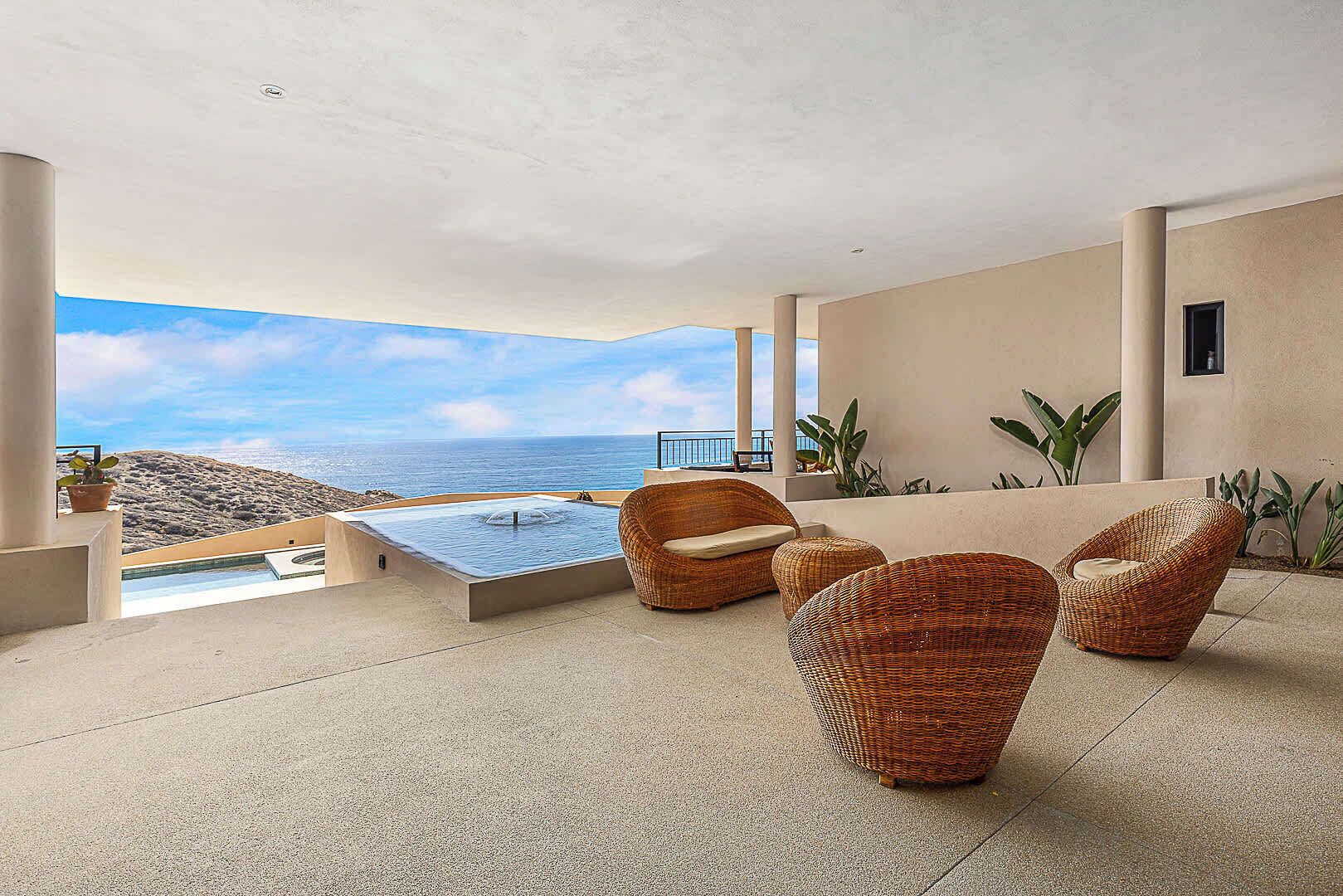 A modern outdoor lounge area with a hot tub, wicker furniture, and a view of the ocean.