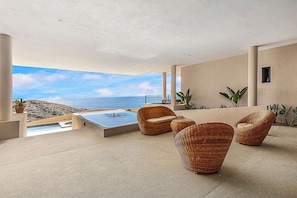 A modern outdoor lounge area with a hot tub, wicker furniture, and a view of the ocean.