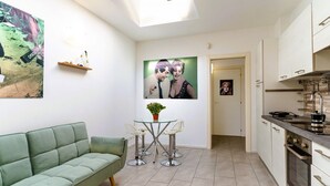 A modern kitchen with white cabinets, a dining area with a glass table and chairs, and a green sofa. - GuestHost - Casa Cabiria Apartment (Torino)