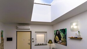 A room with a skylight, a door, a small window, a wall-mounted light, a painting, and a shelf with decorative items. - GuestHost - Casa Cabiria Apartment (Torino)