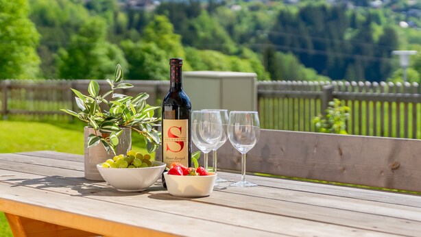 A wooden picnic table with a bottle of wine, two glasses, a bowl of grapes, and a potted plant. - Beautiful chalet near the Nassfeld skiing area (Obermöschach)