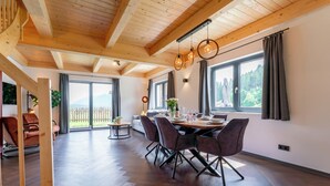 Un'ampia sala da pranzo con un tavolo in legno apparecchiato per quattro persone, ampie finestre con tende e vista sul verde.