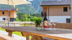 A wooden table with a bottle of wine, two glasses, and bowls of strawberries and grapes.