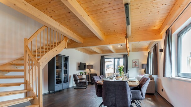 A spacious dining area with a wooden staircase, a dining table set for four, and a modern kitchen in the background.