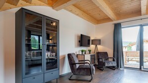 A modern living room with a wooden ceiling, a built-in cabinet with glass doors, a flat-screen TV, and two leather armchairs.