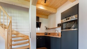 Een moderne keuken met donkere kastjes, een houten trap en een inbouwmagnetron.