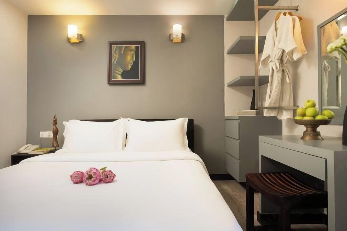 Une chambre d’hôtel comprenant un lit, une table de chevet, une commode et un miroir, ainsi qu’un peignoir et un panier de fruits.