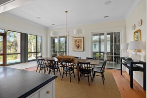A spacious dining area with a large table and chairs, a hanging light fixture, and a view through glass doors.