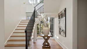 A staircase with wooden steps and black railings, leading to a room with a large window and a wall-mounted abstract painting. - Luxe Interiors + Pool and Views overlooking Marsh (Bluffton)