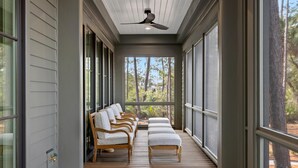 A covered porch with wooden flooring, white cushioned chairs, and a ceiling fan. - Luxe Interiors + Pool and Views overlooking Marsh (Bluffton)