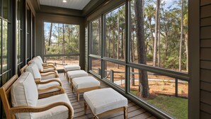 A sunroom with a row of wooden chairs and ottomans, large windows, and a ceiling fan. - Luxe Interiors + Pool and Views overlooking Marsh (Bluffton)