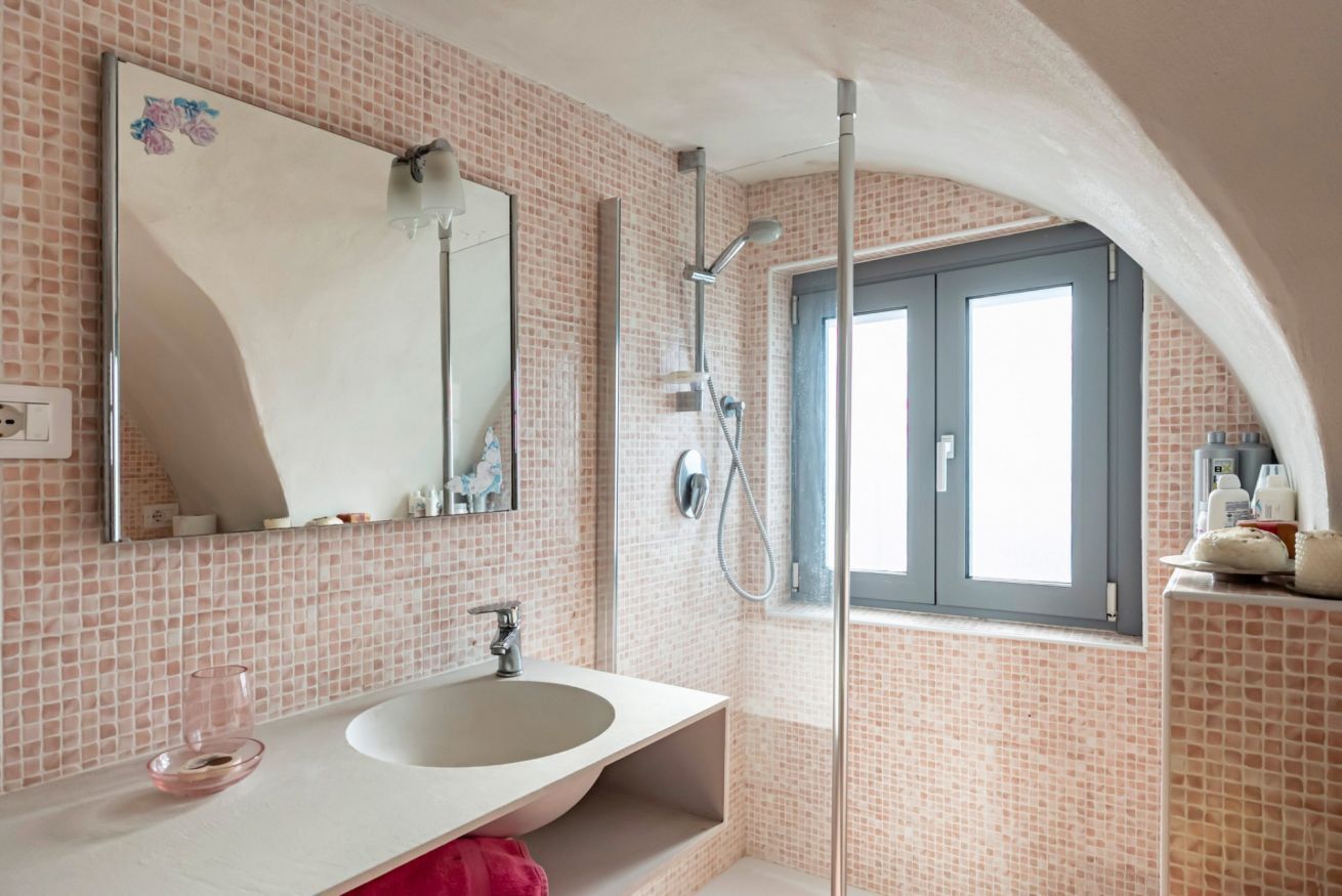 Un baño con lavamanos blanco, un espejo, ducha y ventana.