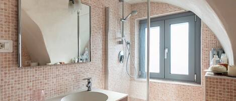 Un baño con lavamanos blanco, un espejo, ducha y ventana.