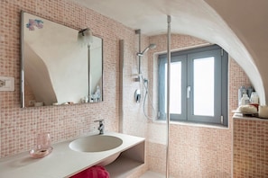 A bathroom with a white sink, a mirror, a shower, and a window.