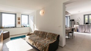 A modern living room with a sofa, a dining area with a table and chairs, and a kitchen with appliances.