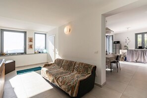 A modern living room with a sofa, a dining area with a table and chairs, and a kitchen with appliances.