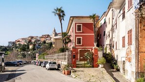 A narrow street lined with traditional buildings, a gated entrance, parked cars, and a clear sky.