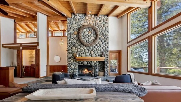 Una sala de estar acogedora con chimenea de piedra, vigas de madera y ventanas amplias.