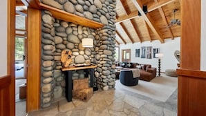 Una chimenea de piedra con repisa de madera, pared de piedra, techo de madera, sofá de cuero marrón y una lámpara.