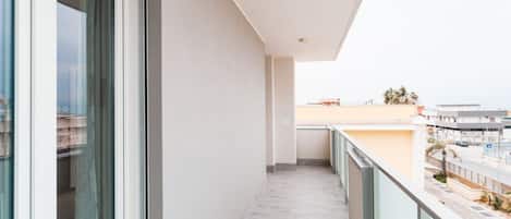 A balcony with a view of a cityscape, a glass door, and a tiled floor.