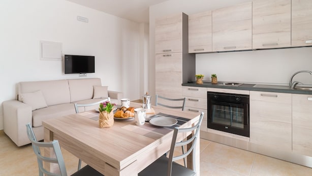 A modern kitchen with light wood cabinets, a built-in oven, and a dining area with a wooden table and chairs. - GuestHost - Scaringi Palace - Room 3A (Trani)