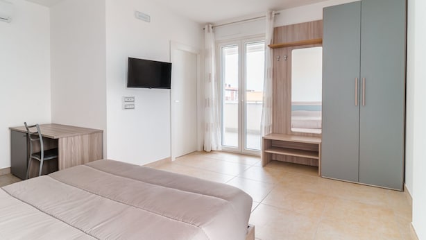 Een slaapkamer met een bed, een bureau, een kledingkast, een televisie en een schuifdeur naar een balkon.